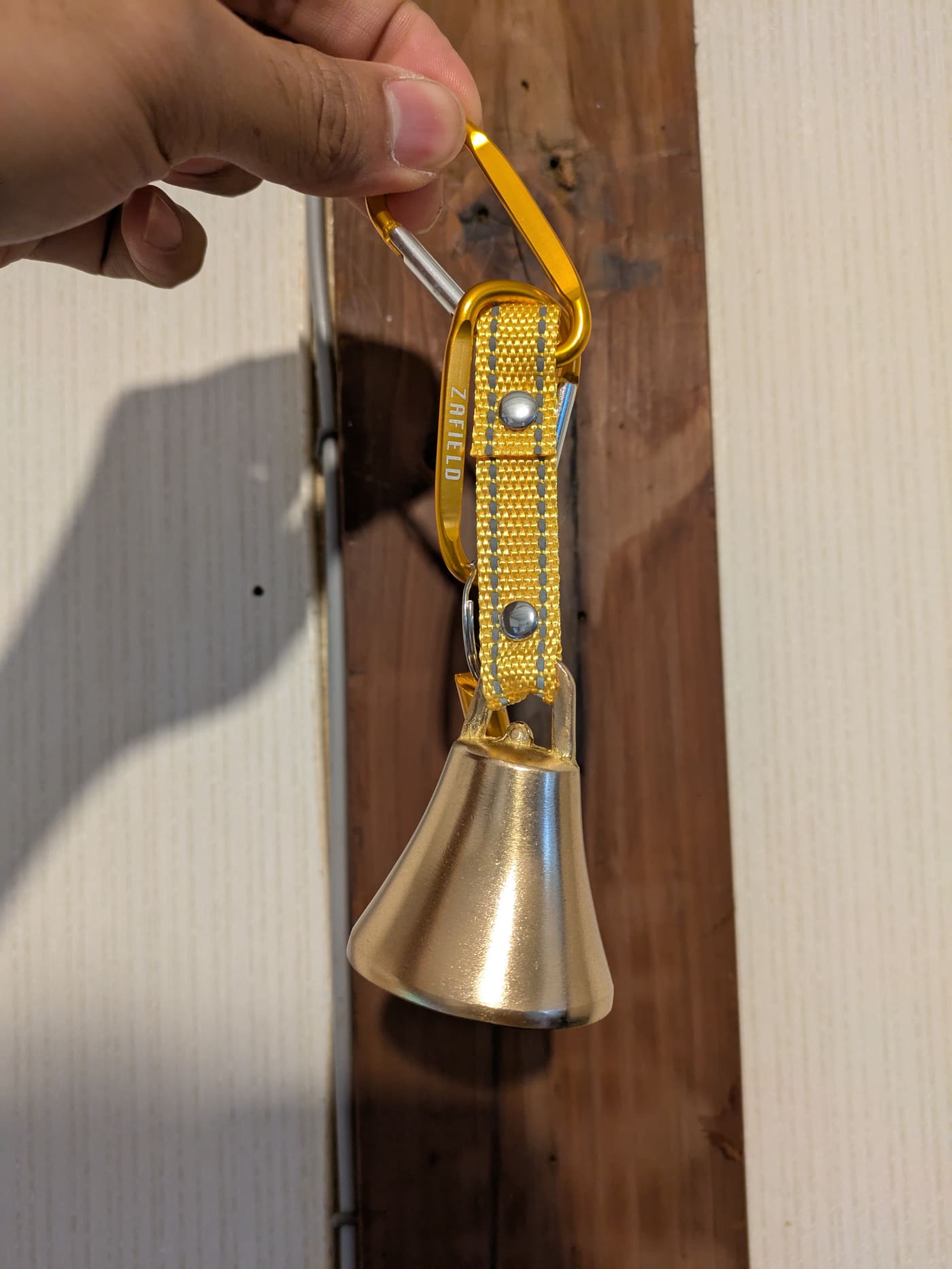 The bear bell — a brass bell on a reflective strap with a carabiner, ready to clip to your bag