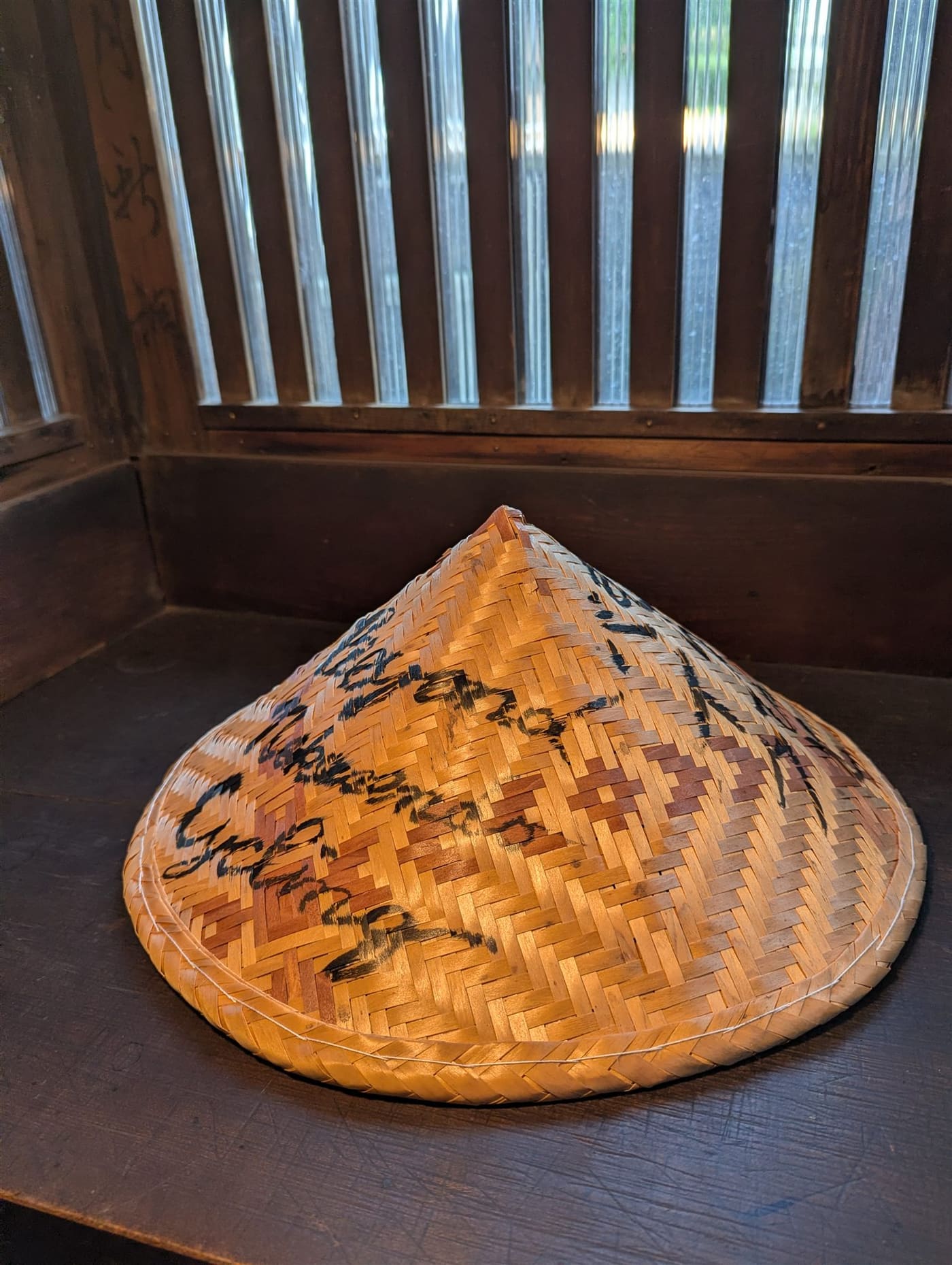 The hinoki travel hat — a woven conical hat with brushed calligraphy, on the guesthouse windowsill