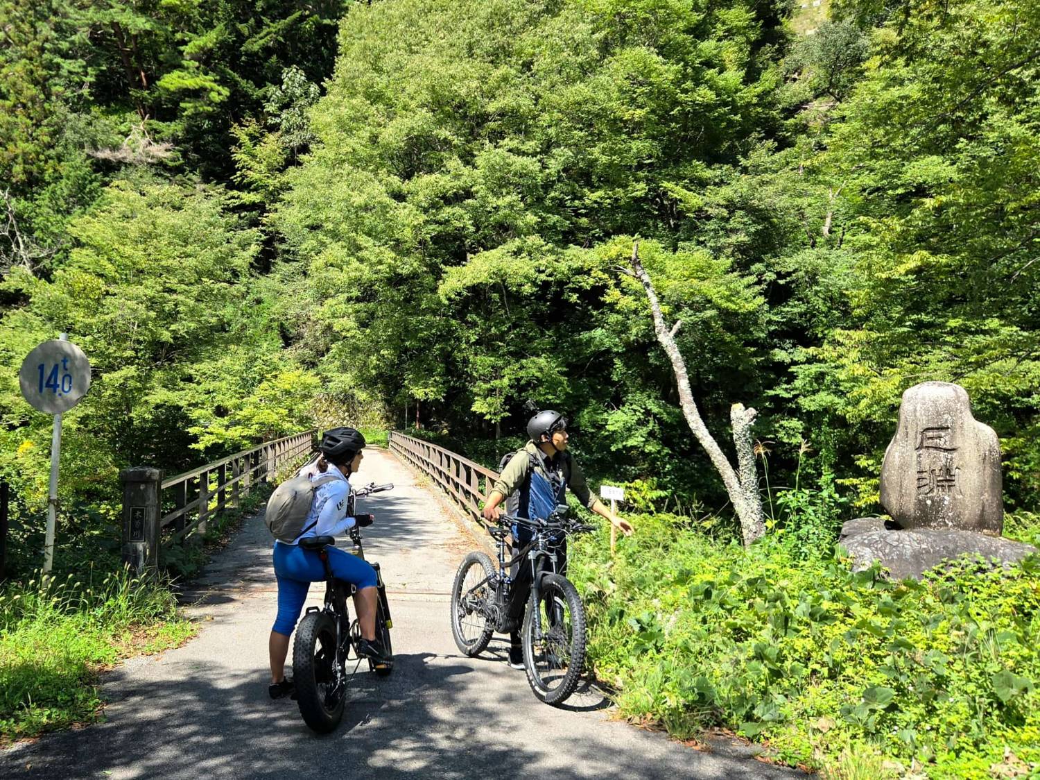 A local guide points out the next stop to a rider at a forest bridge