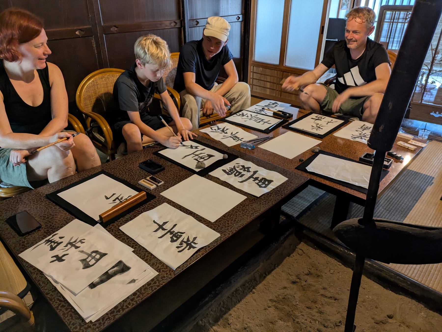 Guests practicing Japanese calligraphy with brush and ink around a low table at Kashiwaya guesthouse