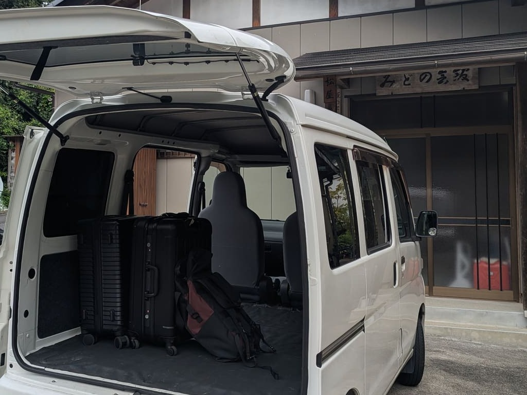 Suitcases loaded in the shuttle van, tailgate open, in front of an old inn